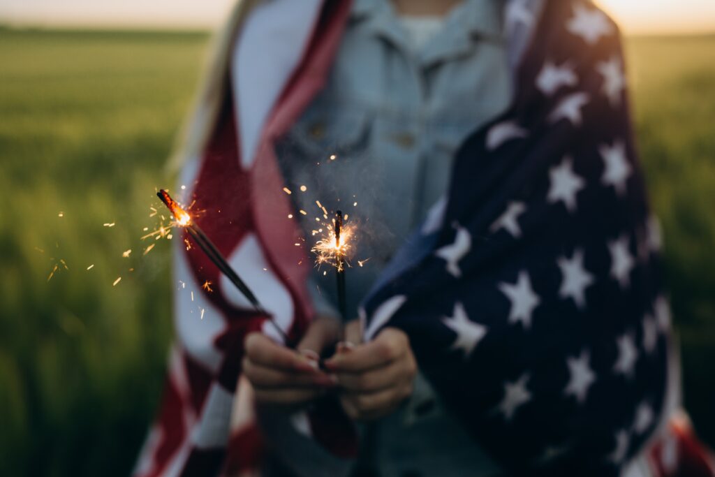 person holding sparklers with the American flag around their shoulders